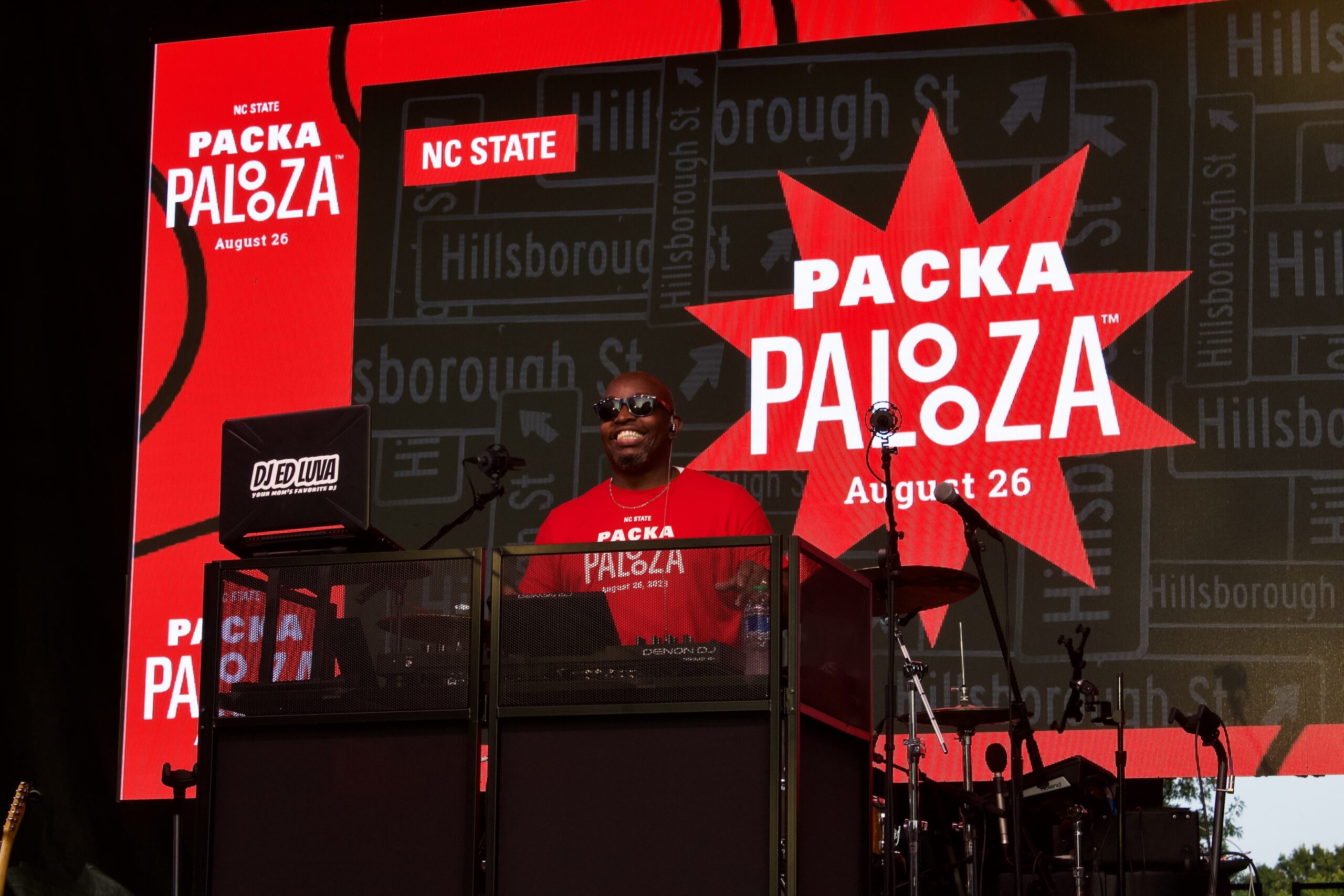 DJ on stage in a red Packapalooza t-shirt with Packapalooza logos in the background.